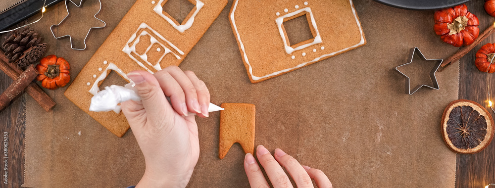 Young woman is decorating Christmas Gingerbread House cookies biscuit at home with frosting topping 