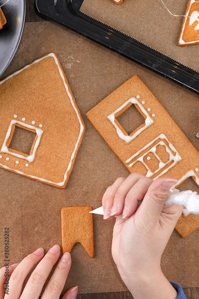 Young woman is decorating Christmas Gingerbread House cookies biscuit at home with frosting topping 