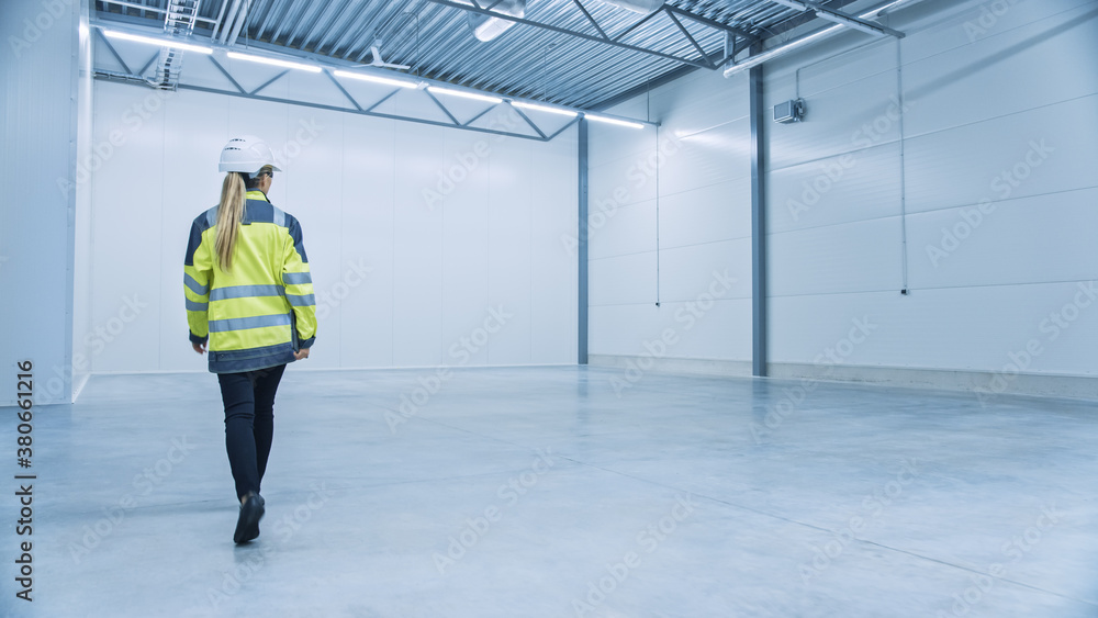 Female Engineer Wearing Safety Hat Walks Across Empty Factory Floor, Inspecting, Planning Machinery 