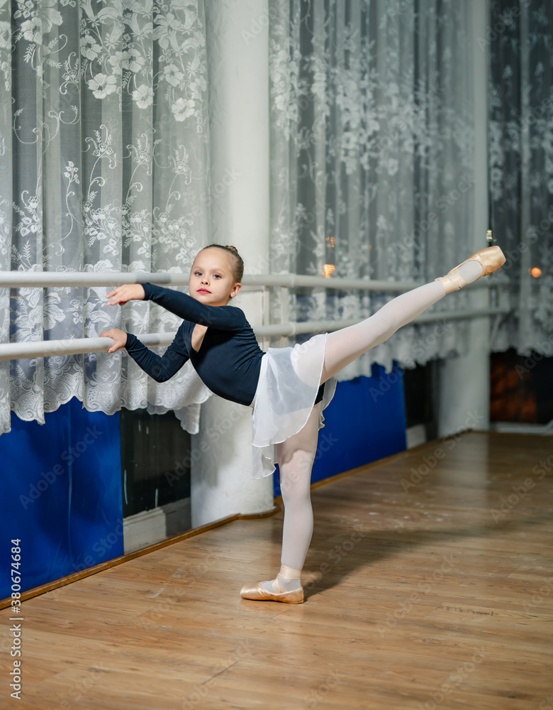 Little ballerina with hair in bunch posing to the camera. Young girl in black costume, white tights 