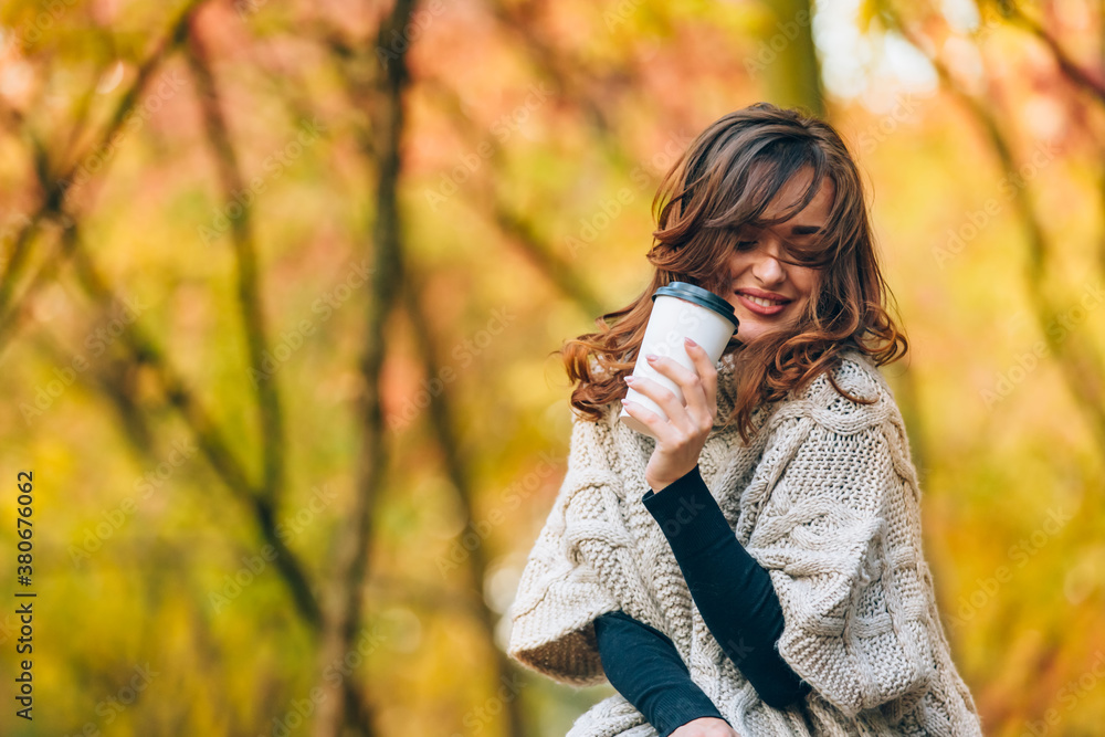 Cute woman with a cup of coffee smiles and looks away. Park in the autumn. Close-up.