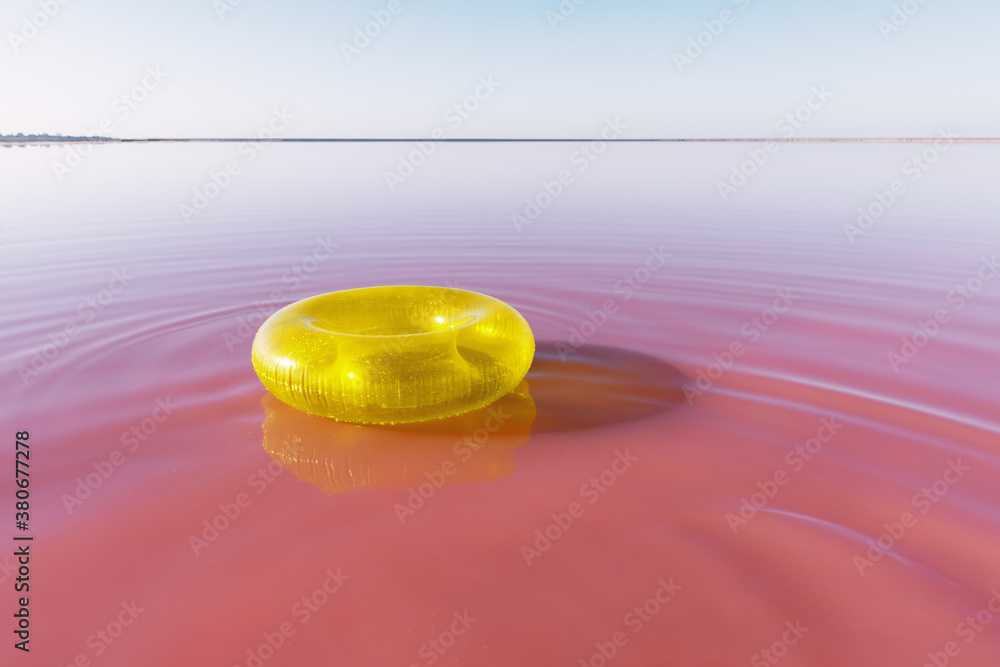 Bright yellow inflatable ring float in pink water lake. Creative color background