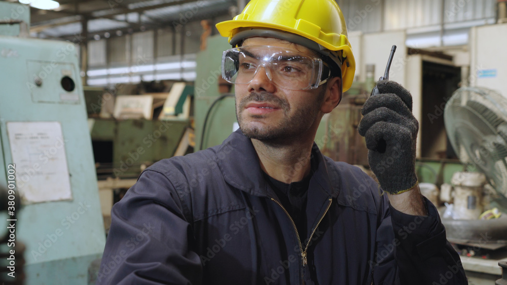 Factory worker talking on portable radio while inspecting machinery parts . Industrial and engineeri