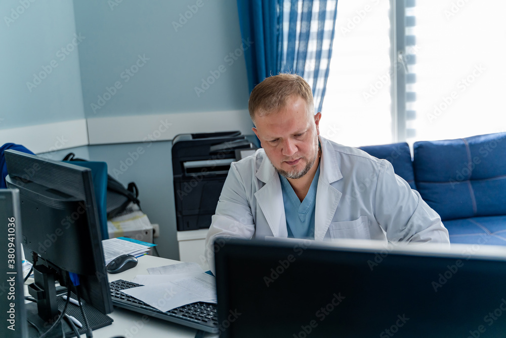 Male doctor in office working at computer. Modern hospital office background.