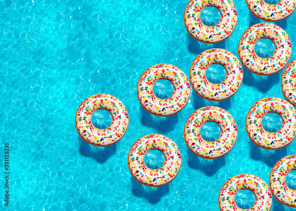 Large group of inflatable candy doughnut buoys swim in the swimming pool view from above