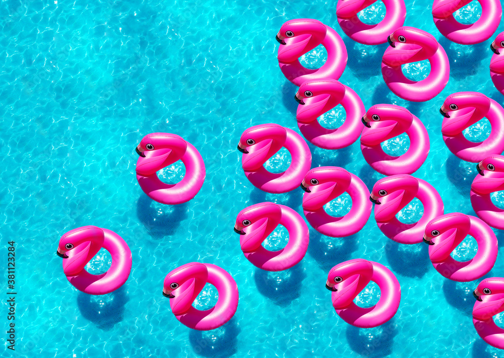 Group of many inflatable flamingo buoys swim in the swimming pool view from above