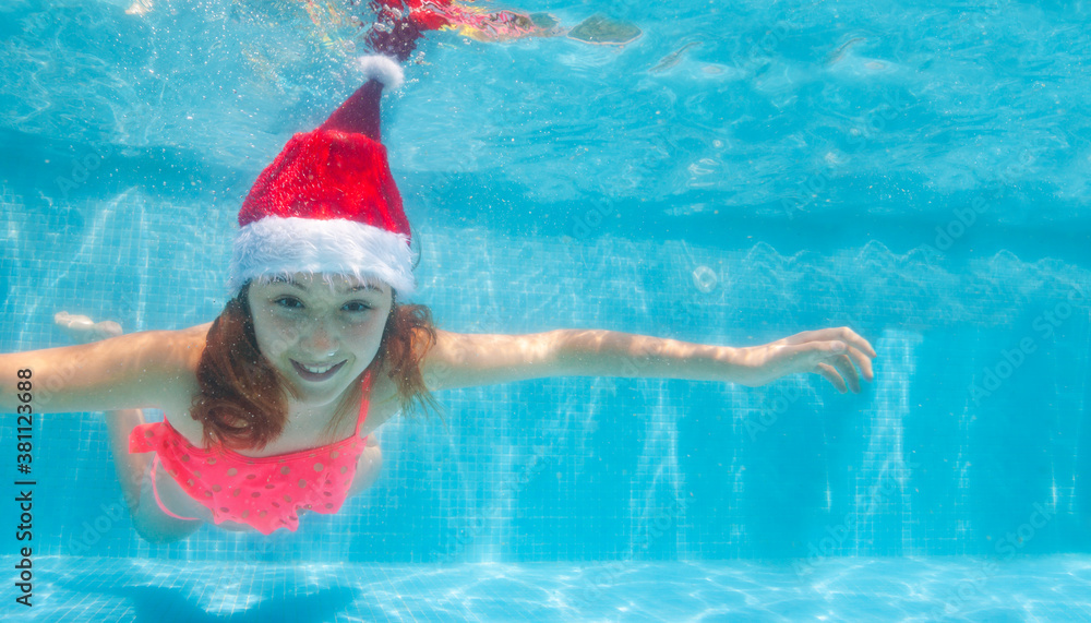 Happy girl dive and swim underwater wearing Santa Claus hat in the pool smile on her Christmas vacat