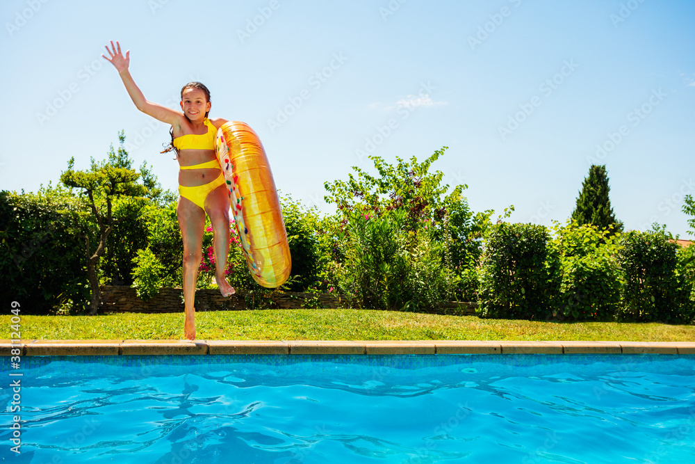 Happy teenage girl with inflatable doughnut buoy run and jump in the swimming pool lifting hand fron