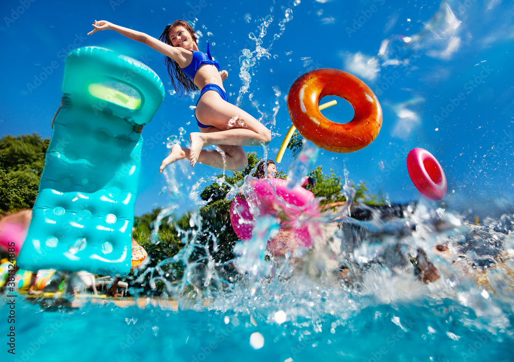 Girl in a group of teenage children have fun in the swimming pool diving with inflatable toys doughn