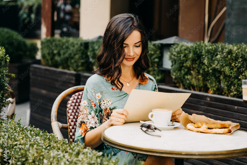 Young happy woman sitting at a cafe terrace, looking at a menu.