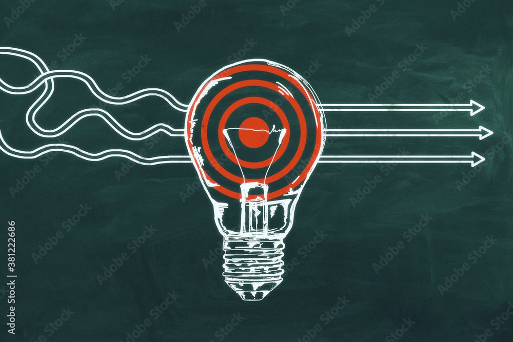 Drawing white arrows with target and lightbulb  on blackboard.