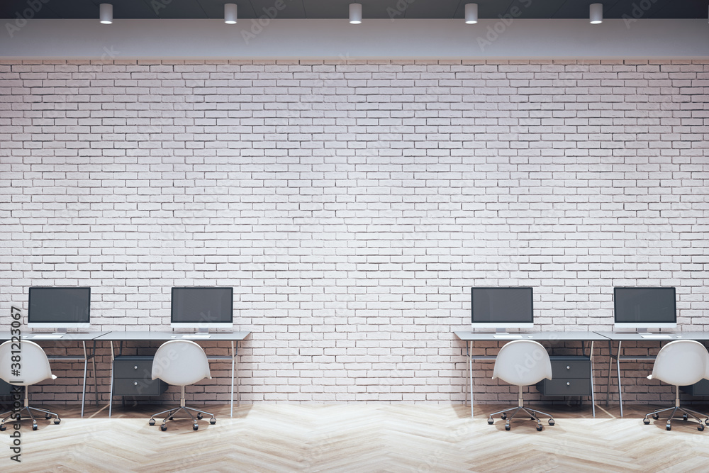 Modern workplace room with computers on table and blank brick wall.