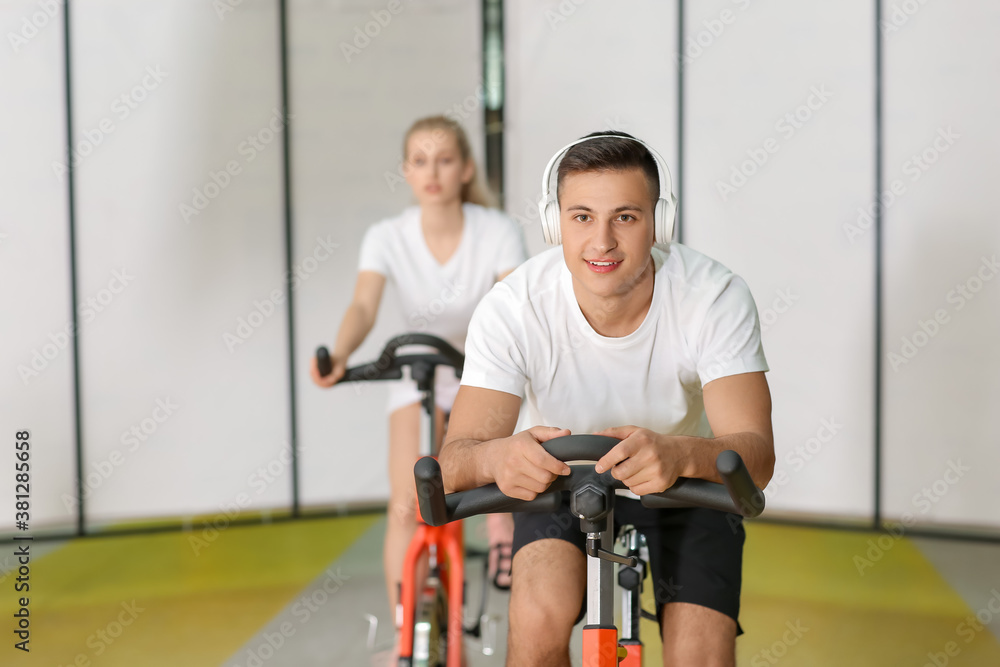 Young man training on exercising bike in gym