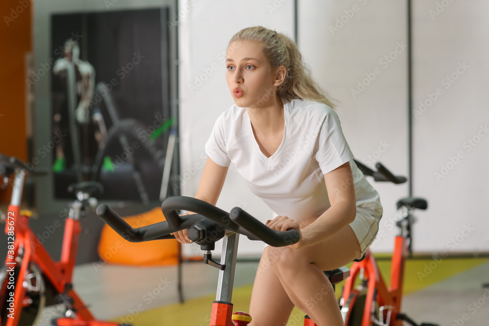 Young woman training on exercising bike in gym