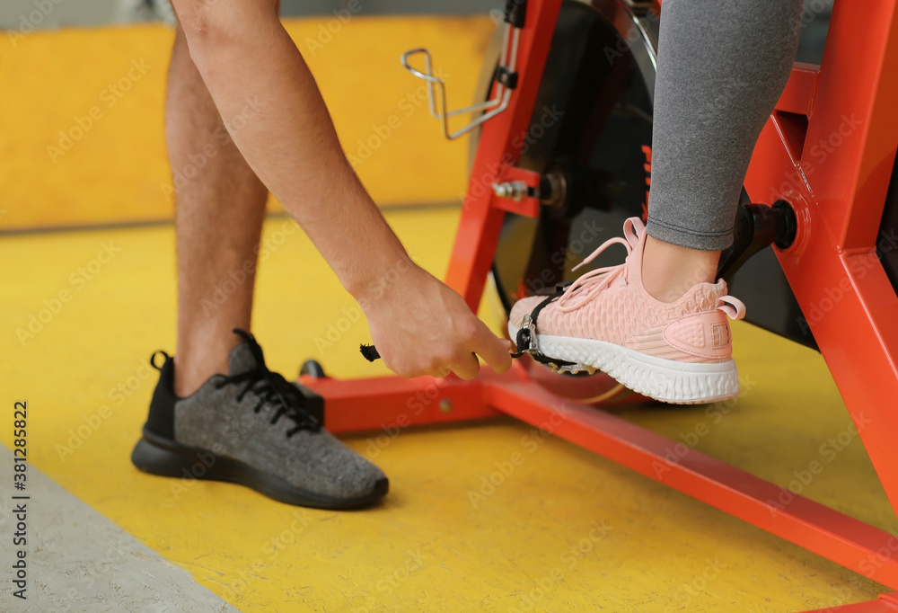 Young woman with coach training on exercising bike in gym