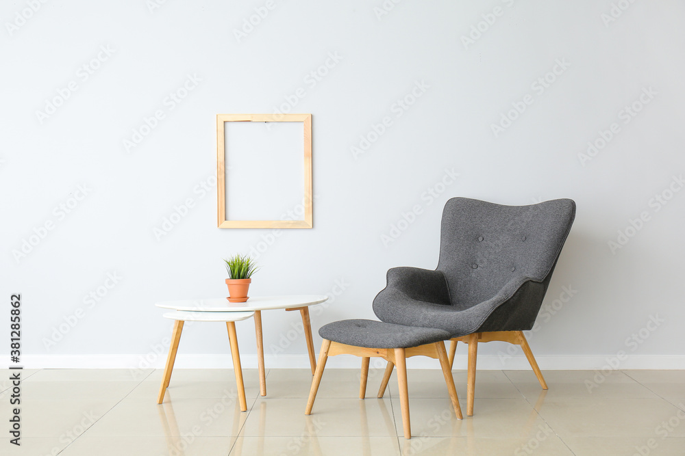 Stylish armchair and ottoman with table near light wall in room