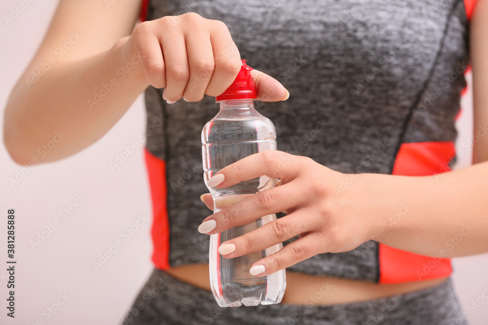 Sportswoman with bottle of fresh water on grey background, closeup