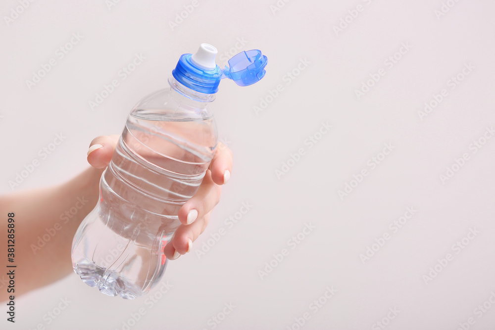 Female hand with bottle of water on light background