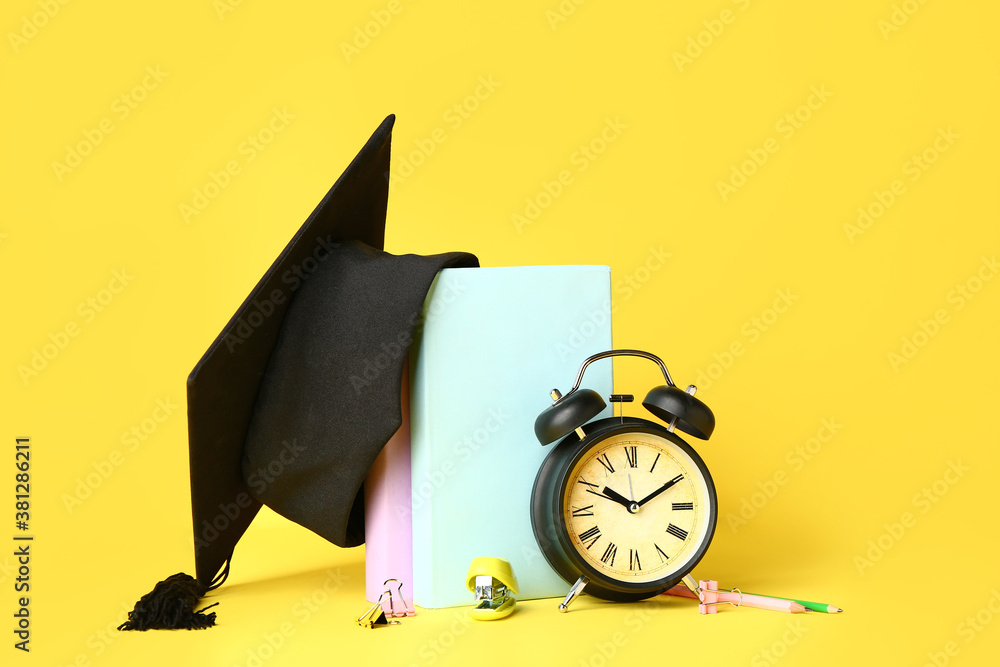 Graduation hat, alarm clock and stationery on color background