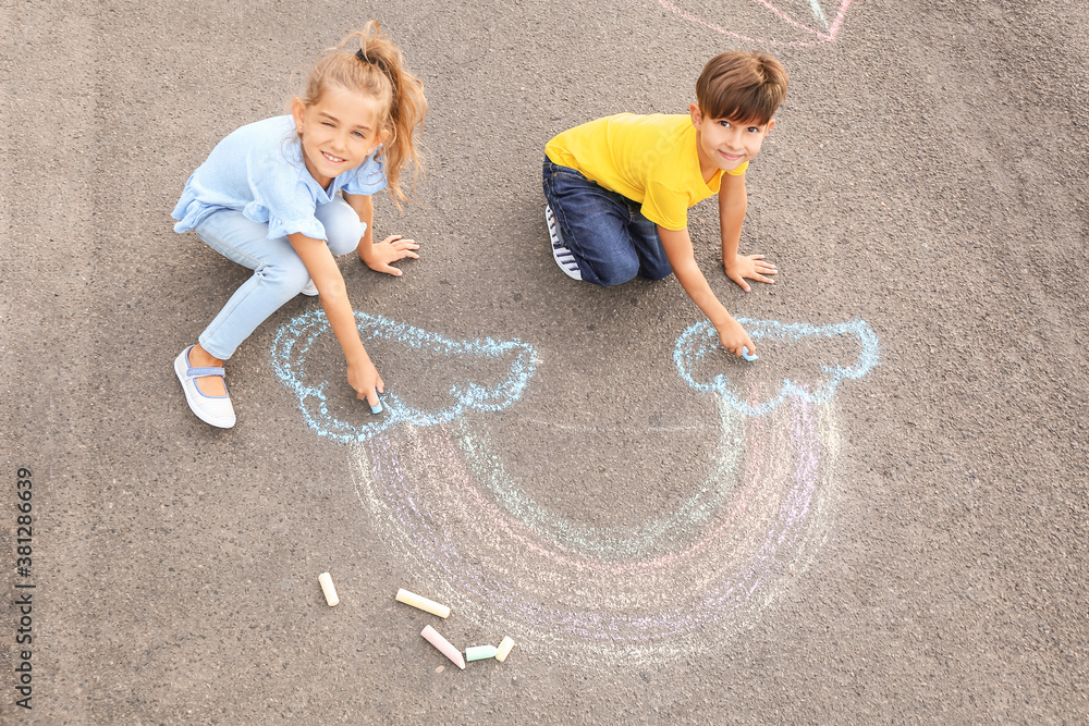 Little children drawing rainbow with chalk on asphalt