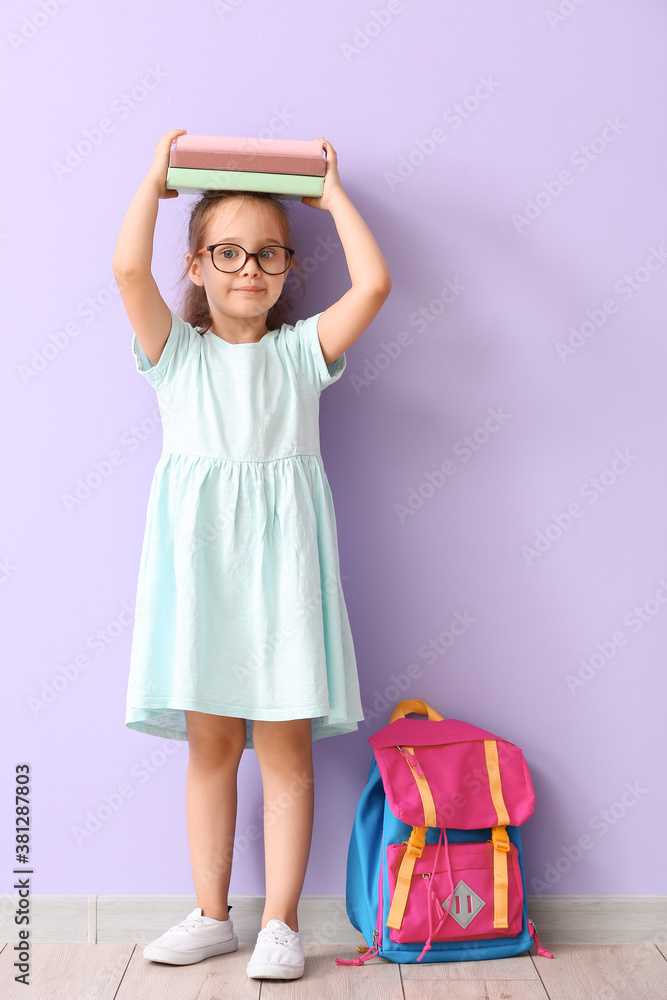 Little schoolgirl with books near color wall