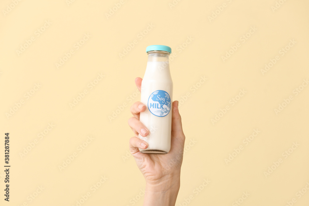 Female hand with bottle of soy milk on color background