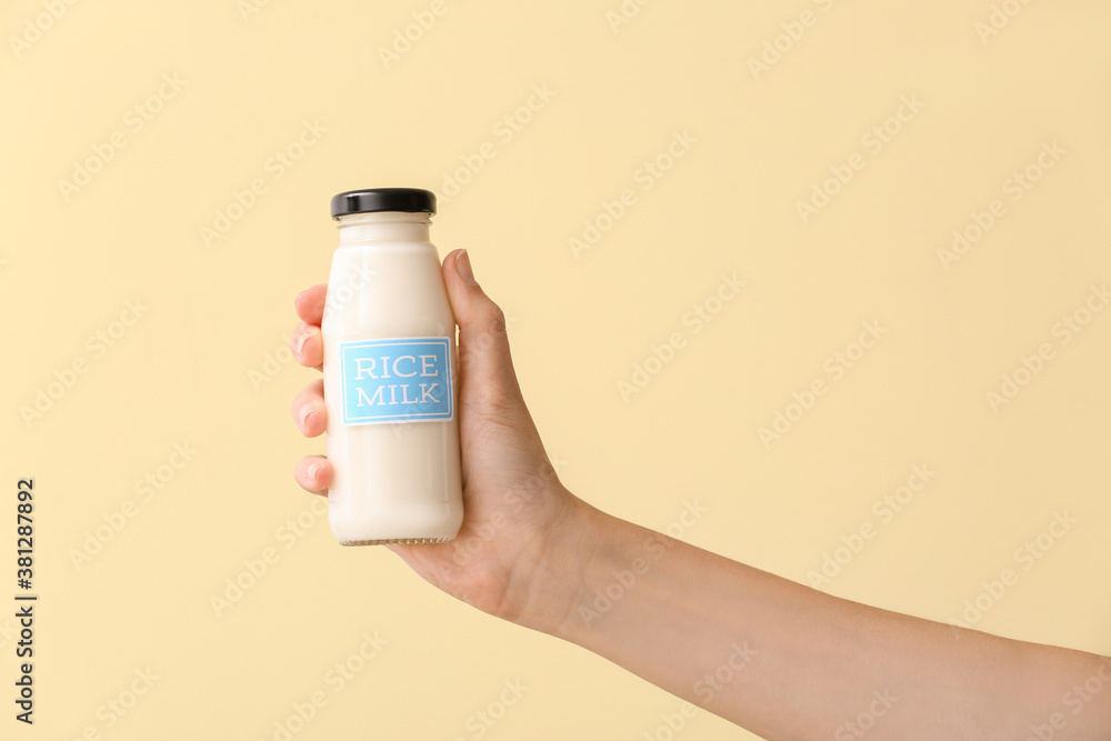 Female hand with bottle of rice milk on color background