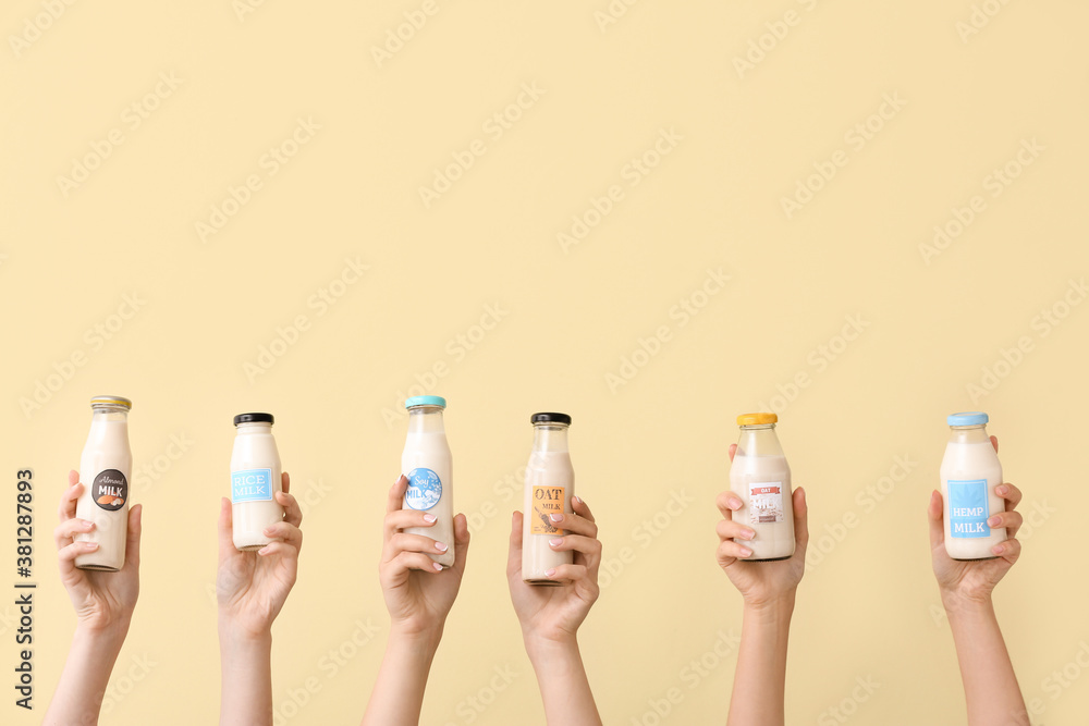 Female hands with bottles of vegan milk on color background