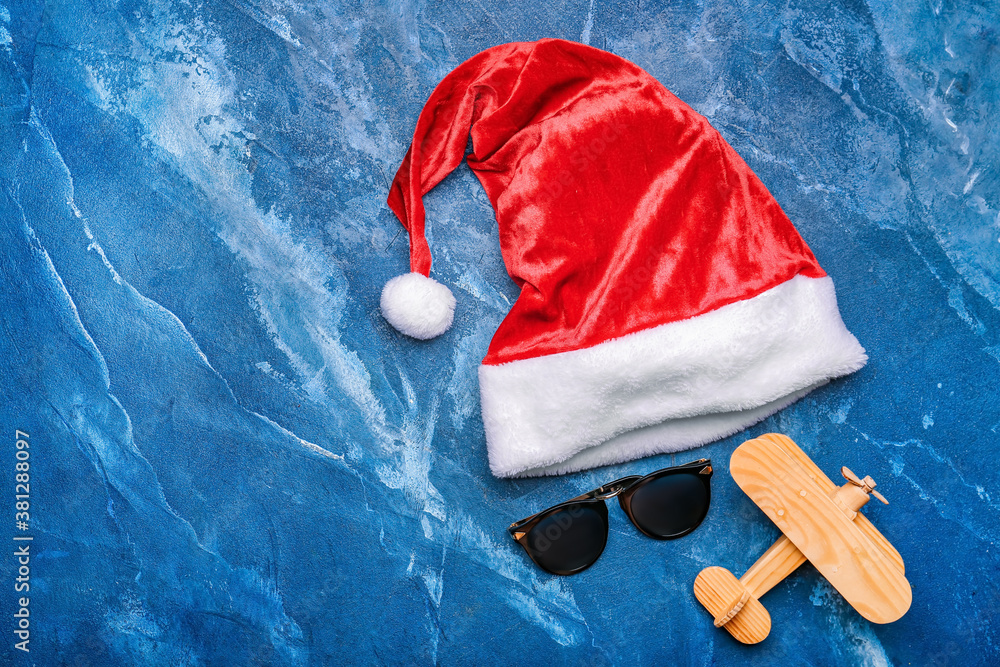 Santa Claus hat with sunglasses and airplane on color background