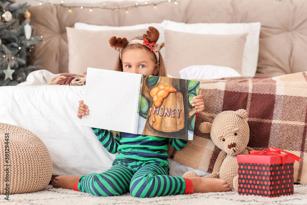 Cute little girl reading book at home on Christmas eve