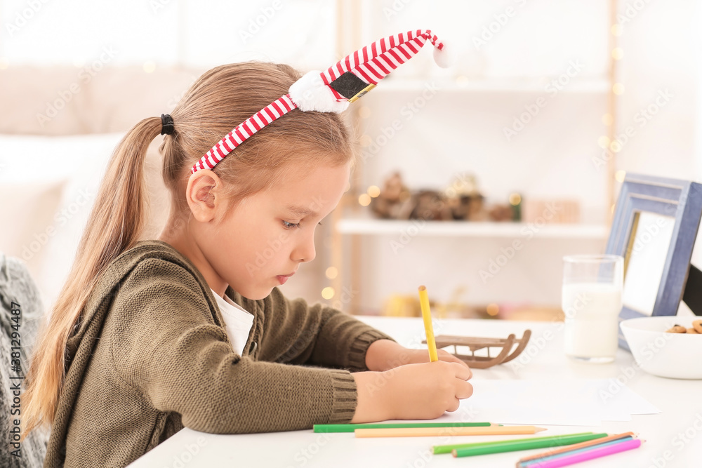 Cute little girl writing letter to Santa Claus on Christmas eve at home