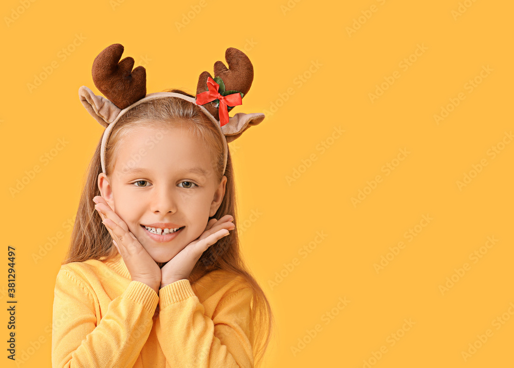 Cute little girl with deer horns on color background