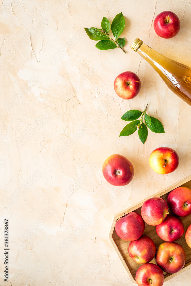 Apple cider vinegar in glass bottle and wooden tray with red apples