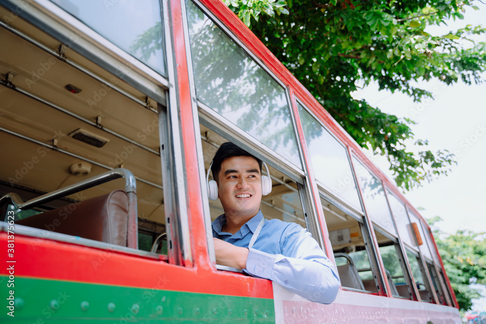 Asian man using smartphone listen to music with wireless headphone on a bus in Bangkok.