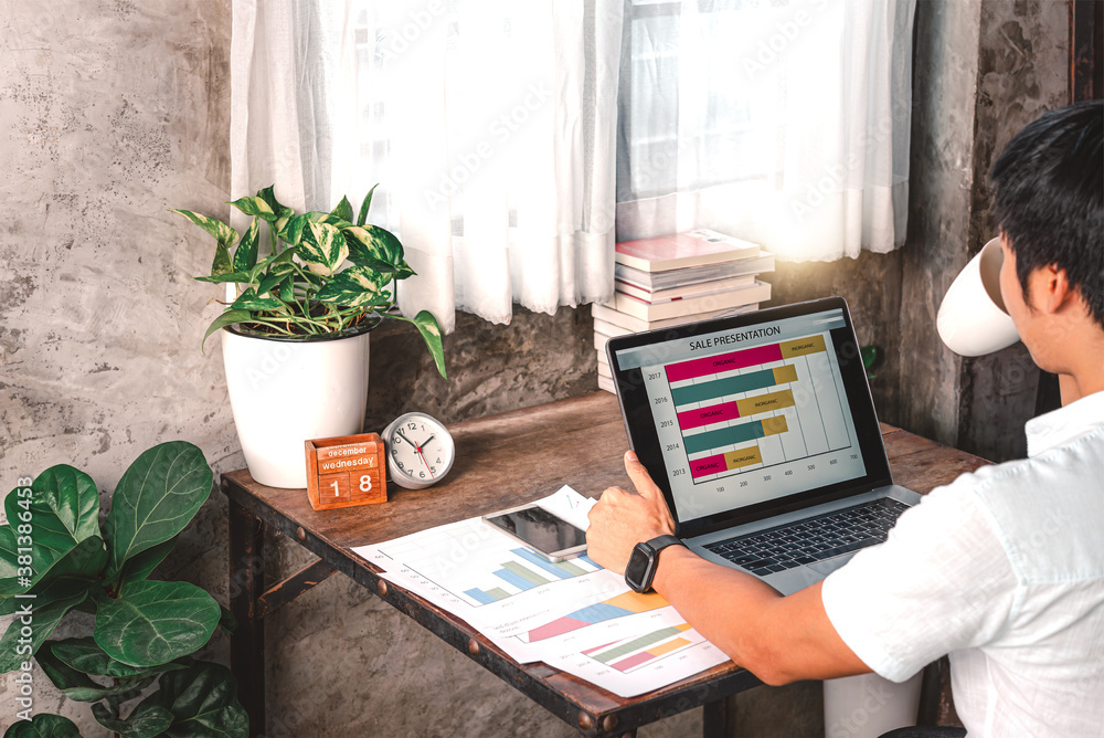 A man was working from home with a laptop ,paper sheet while drinking a cup of coffee.