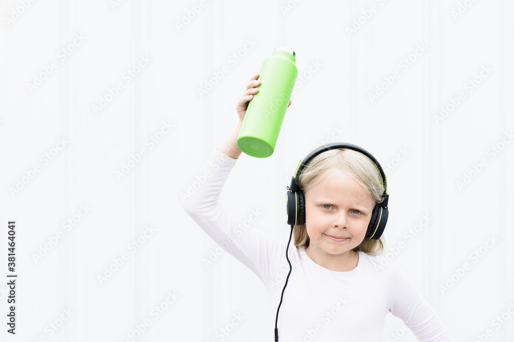 Young blond girl on white background drink fresh spring water from green reusable bottle. Healthy li