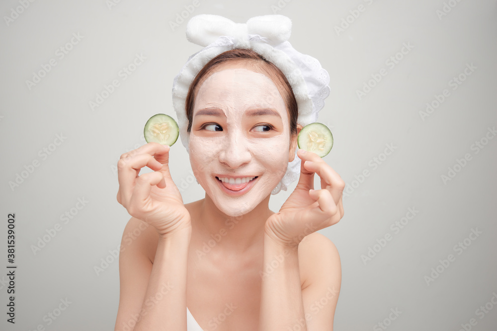 Beautiful girl holding a slice of cucumber in front of her face with mask of clay.