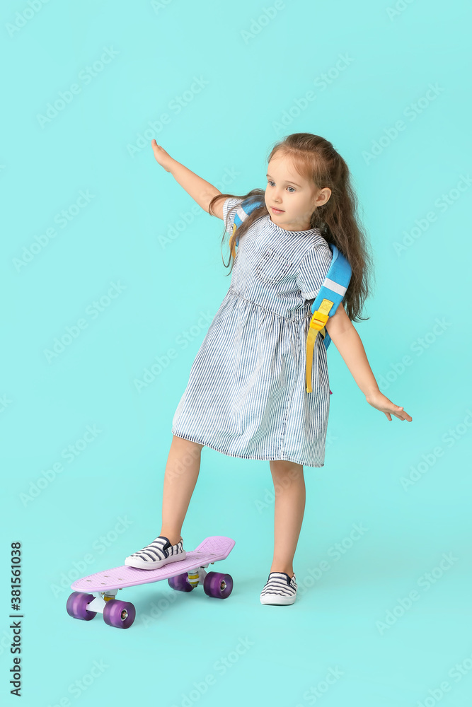 Little schoolgirl with skateboard on color background