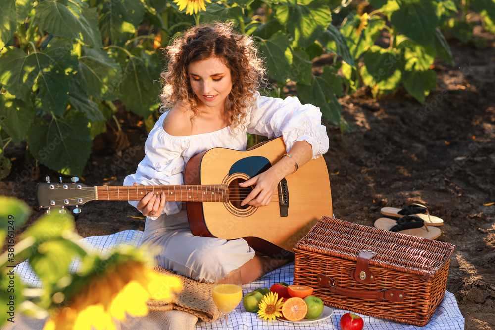 Beautiful young woman playing guitar in sunflower field