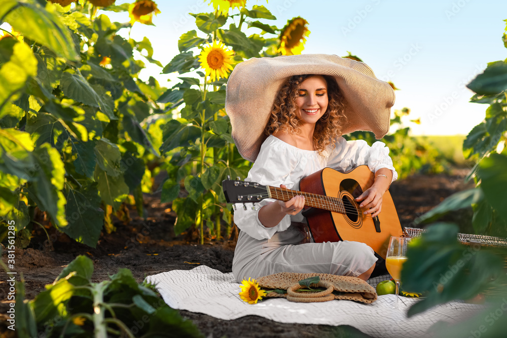 Beautiful young woman playing guitar in sunflower field