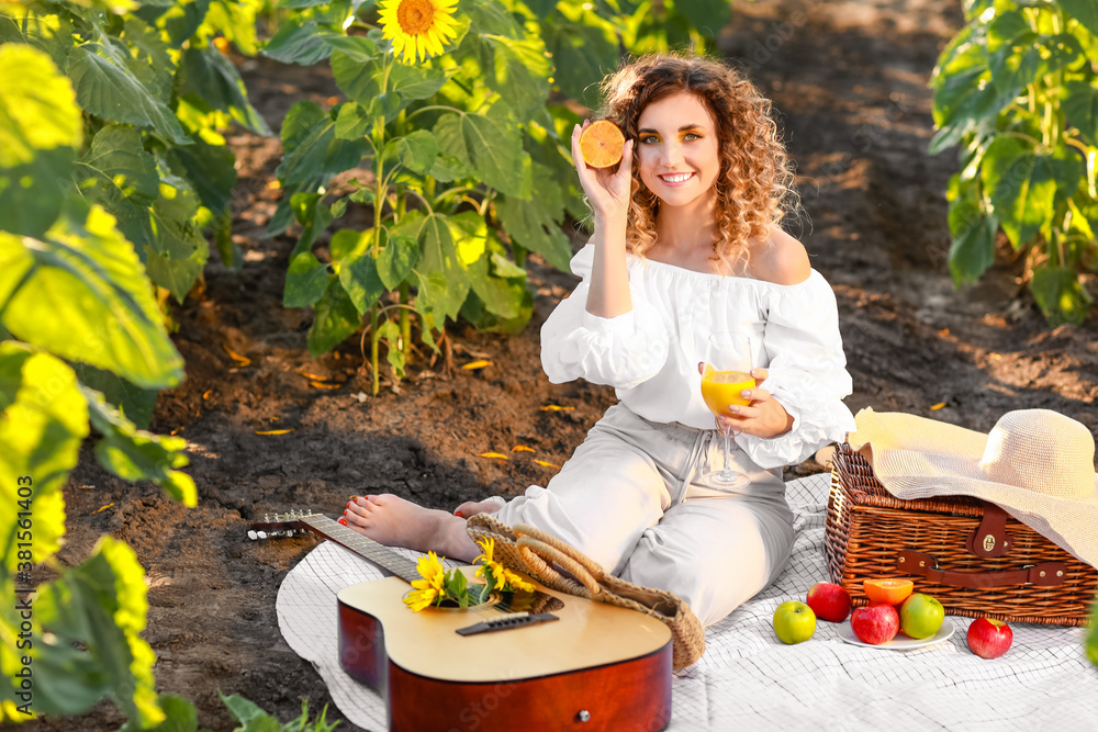 Beautiful young woman with guitar having picnic in sunflower field