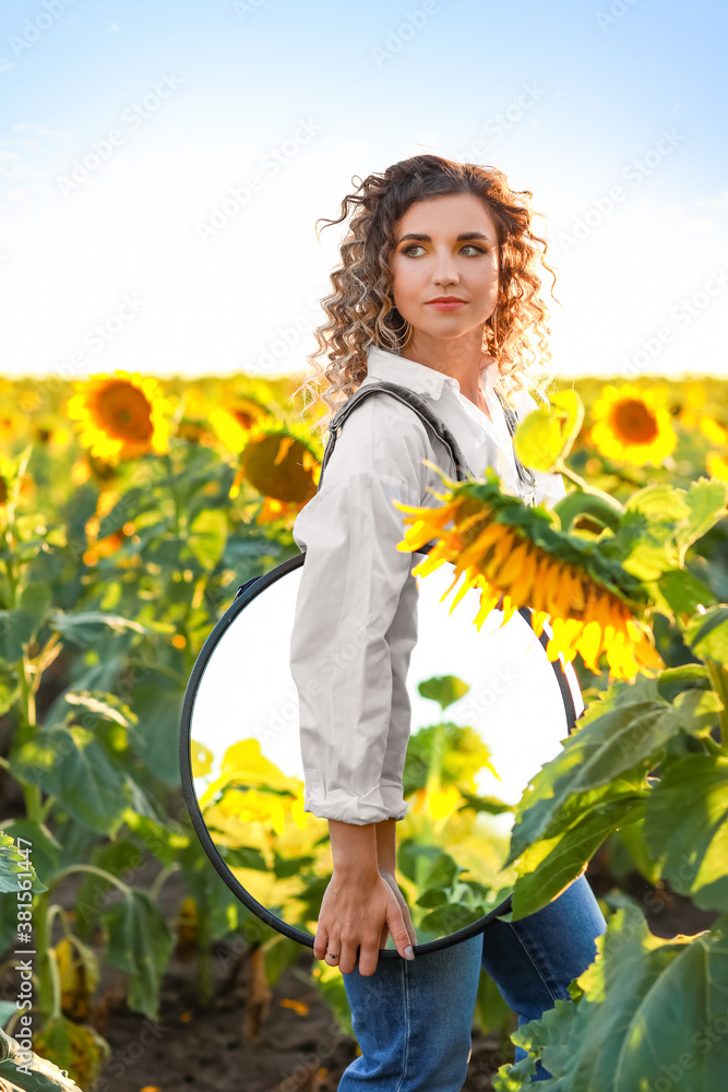 Beautiful young woman with mirror in sunflower field