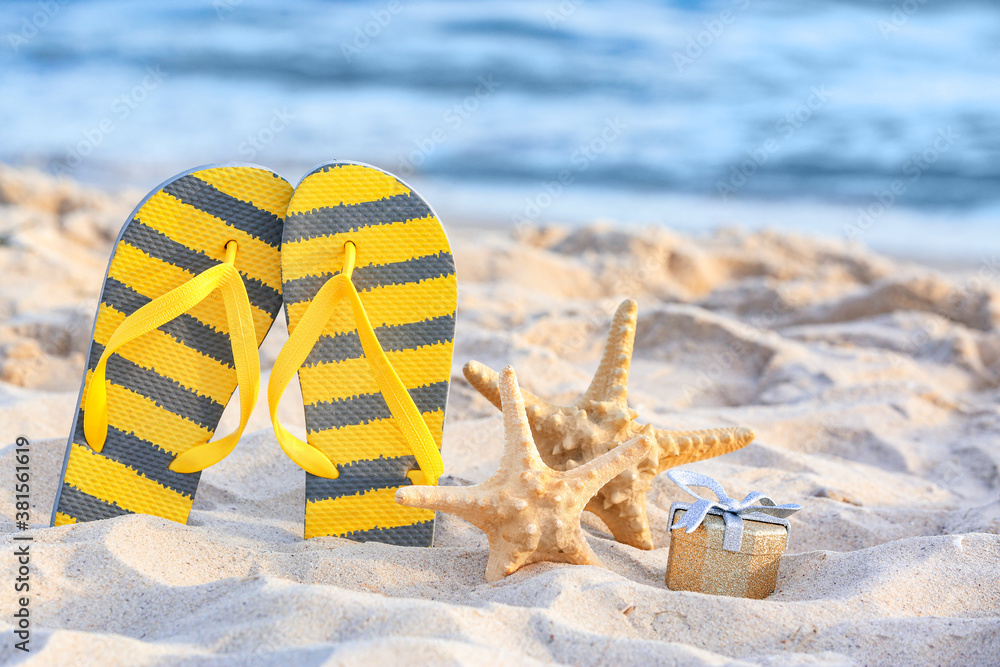 Flip-flops, starfish and gift on beach sand. Christmas vacation concept