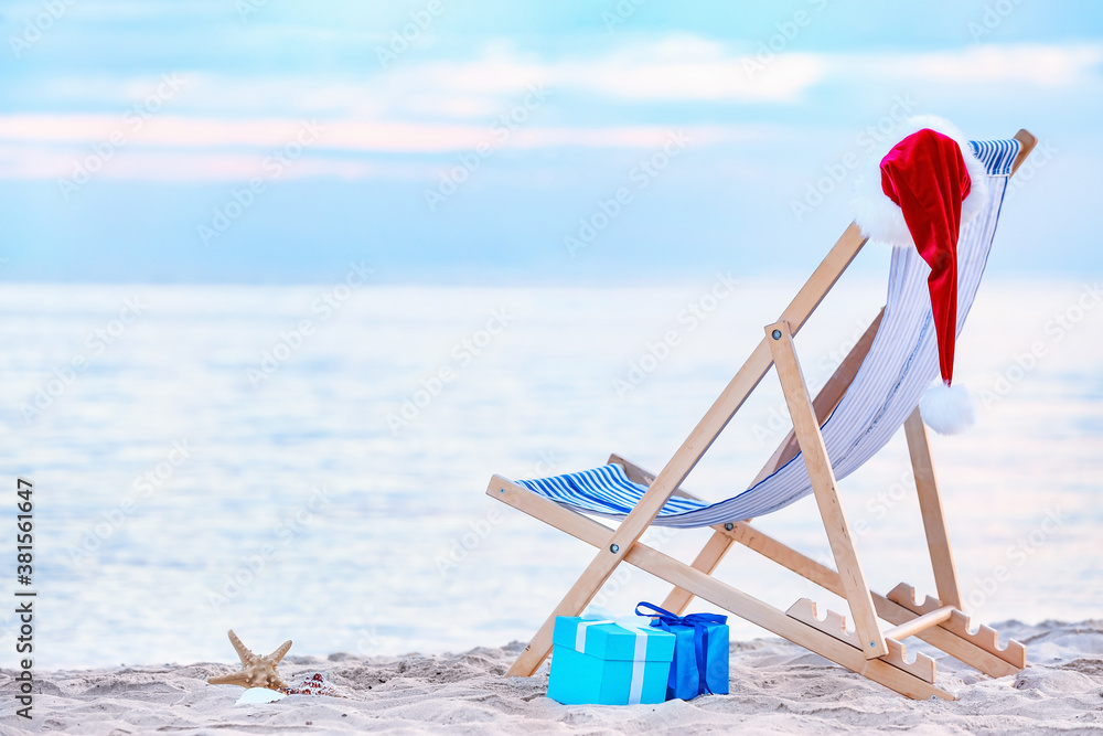 Beach chair, gifts and Santa hat on sea shore. Christmas vacation concept