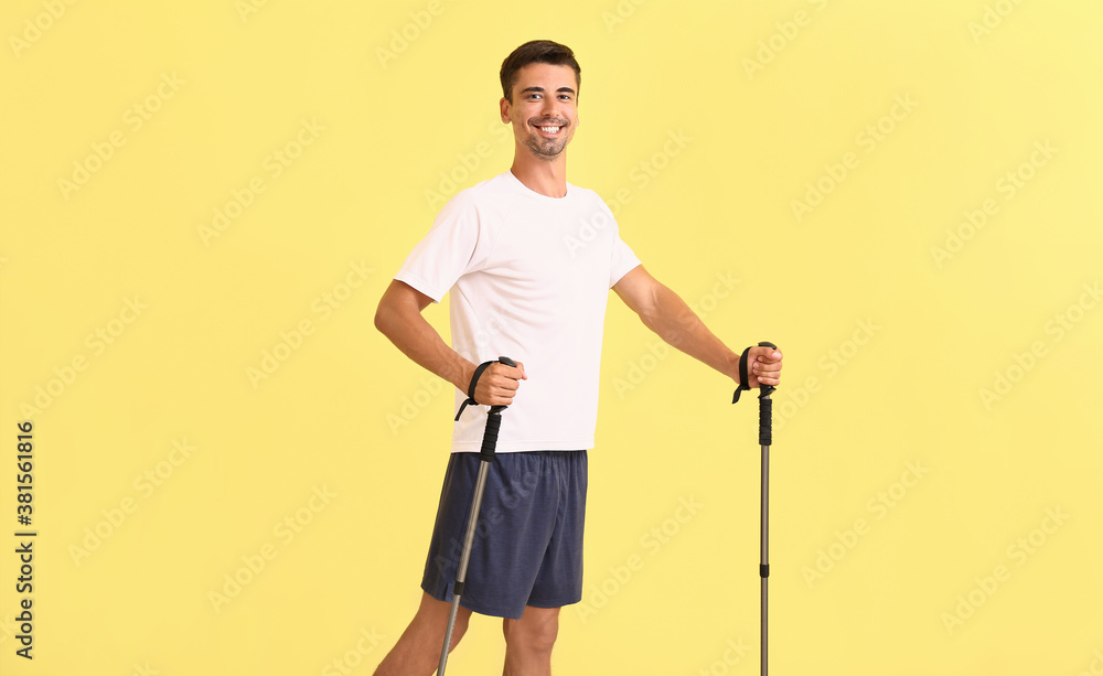 Young man with walking poles on color background