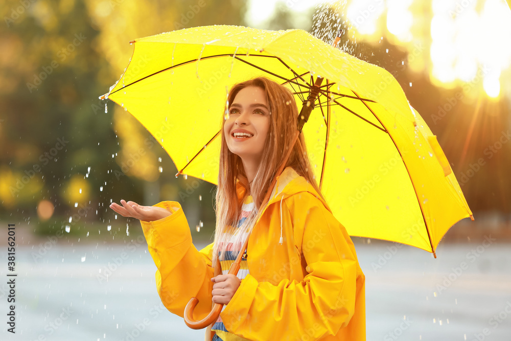 Beautiful young woman with umbrella wearing raincoat outdoors