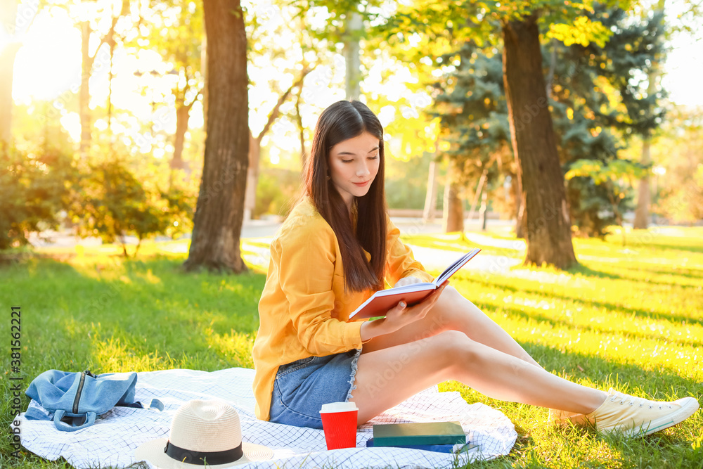 Beautiful young woman reading book in park