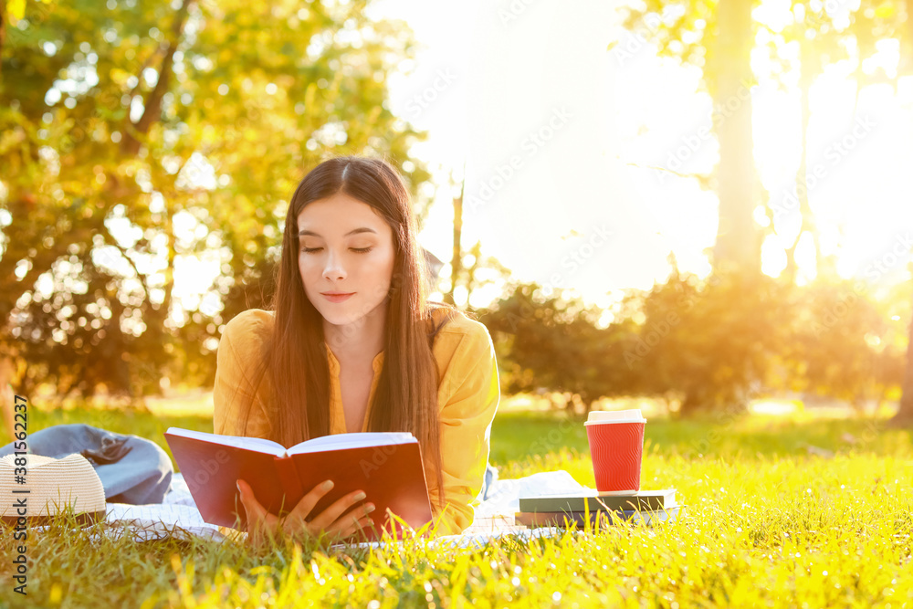 Beautiful young woman reading book in park