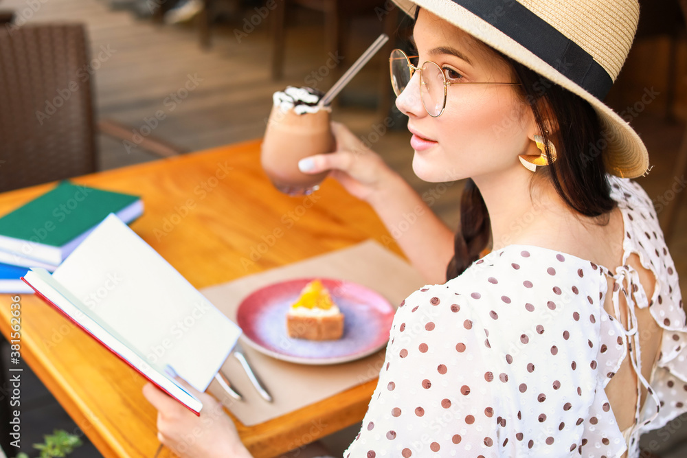 Beautiful young woman reading book in street cafe