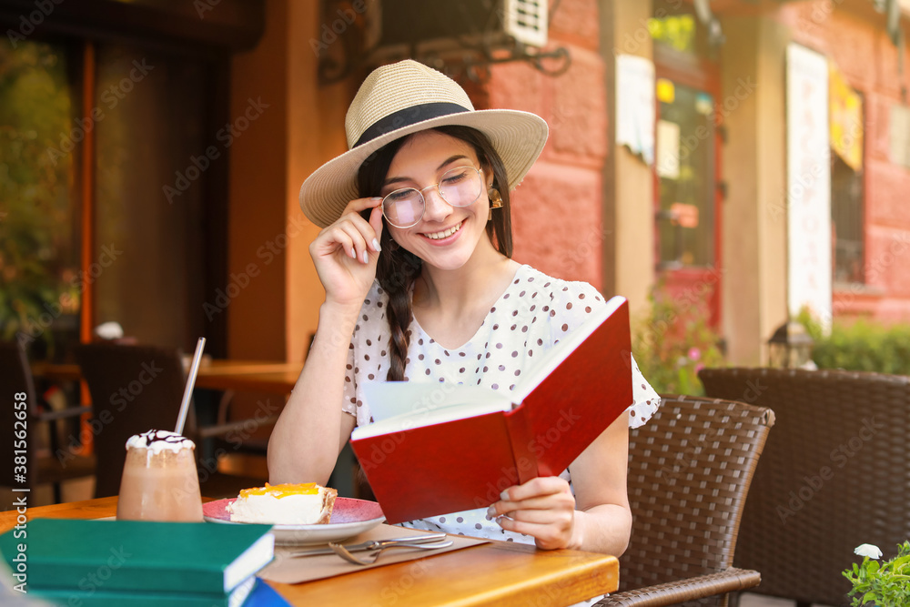 Beautiful young woman reading book in street cafe